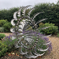 Kinetic metal wind spinner in a flower bed beside a garden path