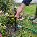 Motion activated deer sprinkler staked beside a flower border