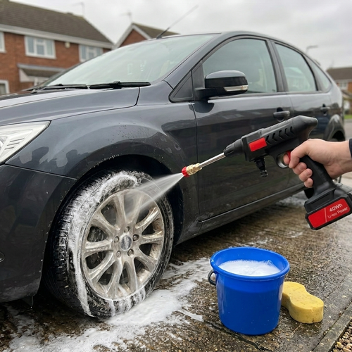 Cordless pressure washer gun rinsing a car on a driveway